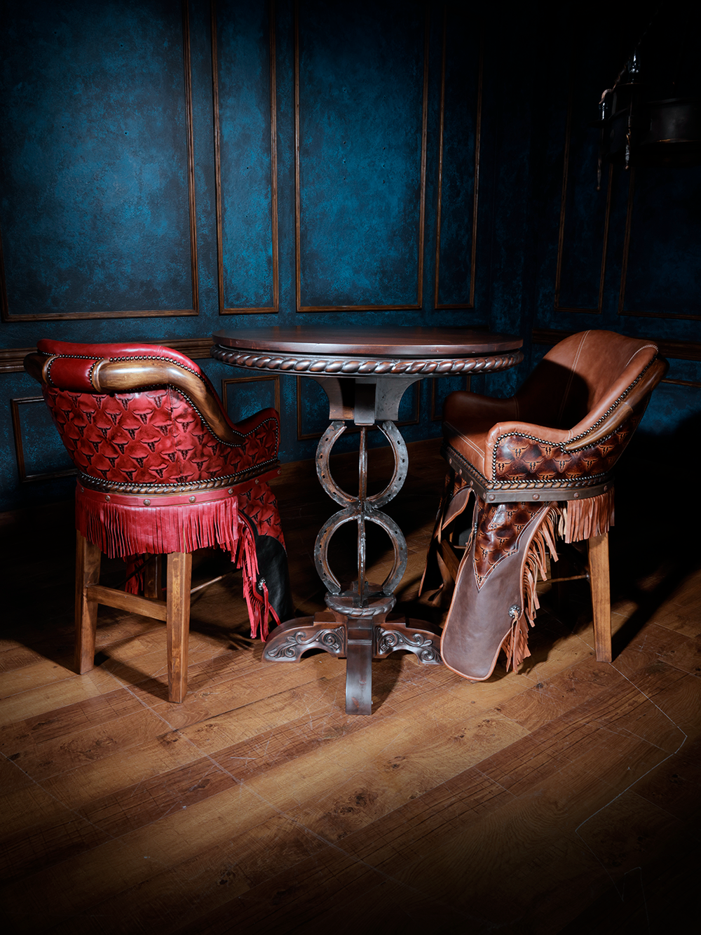 Western pub table with horseshoe base and two leather fringe barstools in red and saddle brown.