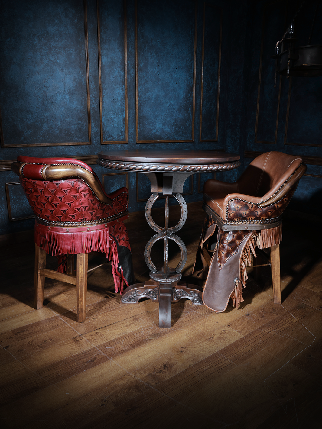 Western pub table with horseshoe base and two leather fringe barstools in red and saddle brown.