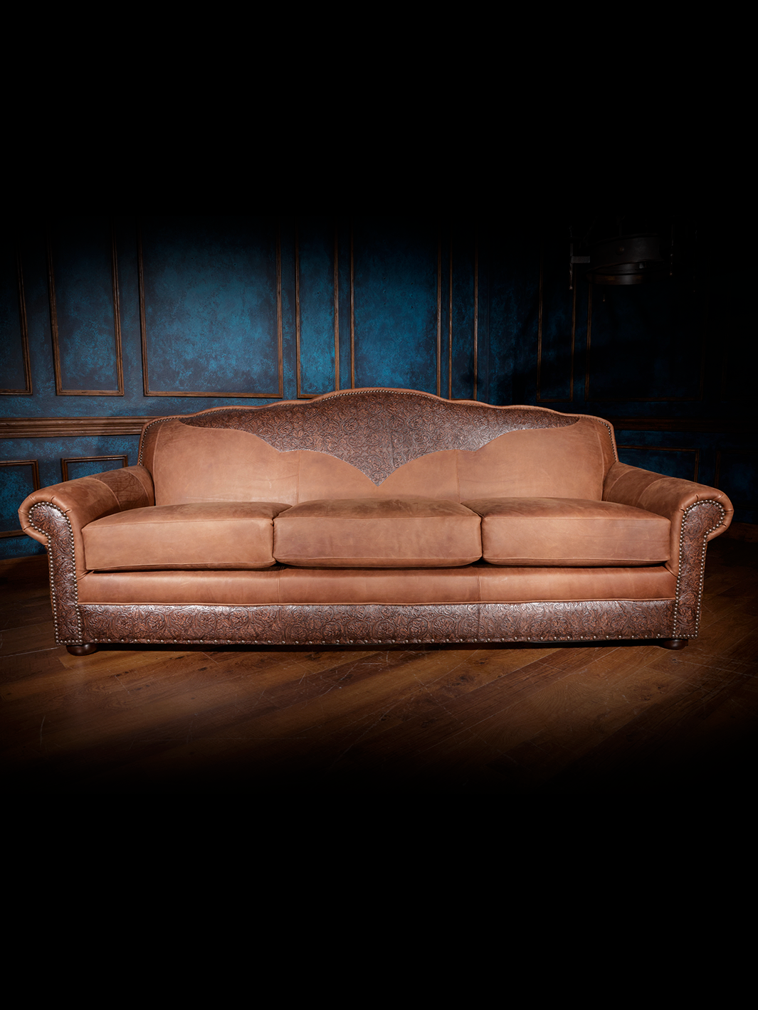 Western-style leather sofa with a three-cushion design, intricate tooled leather detailing across the base and backrest, and rolled arms.
