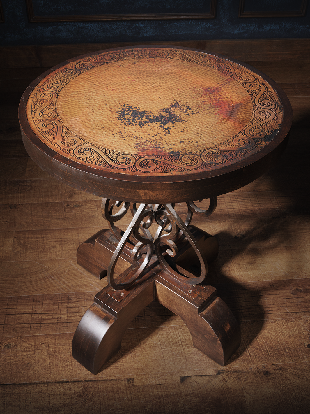 A hand-forged iron base barrel end table with a copper top featuring unique detail, placed on a wooden floor.