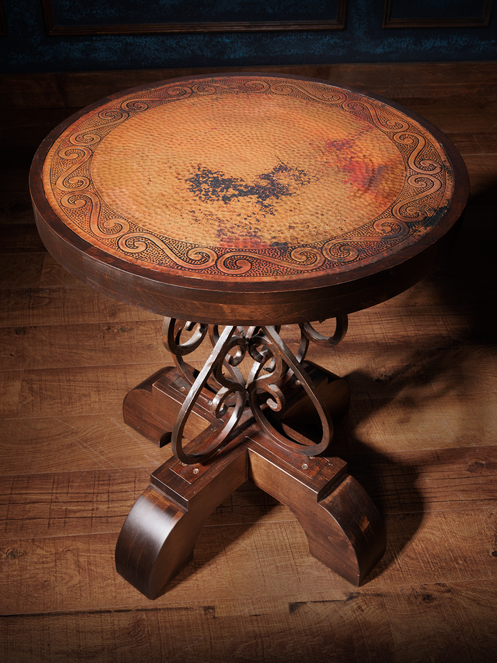 A hand-forged iron base barrel end table with a copper top featuring unique detail, placed on a wooden floor.