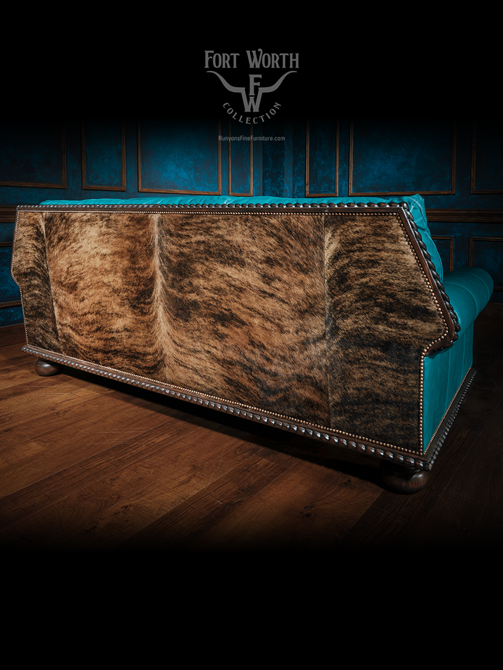Rear view of a turquoise western sofa featuring a cowhide back and detailed nailhead border on a dark carved wooden base.