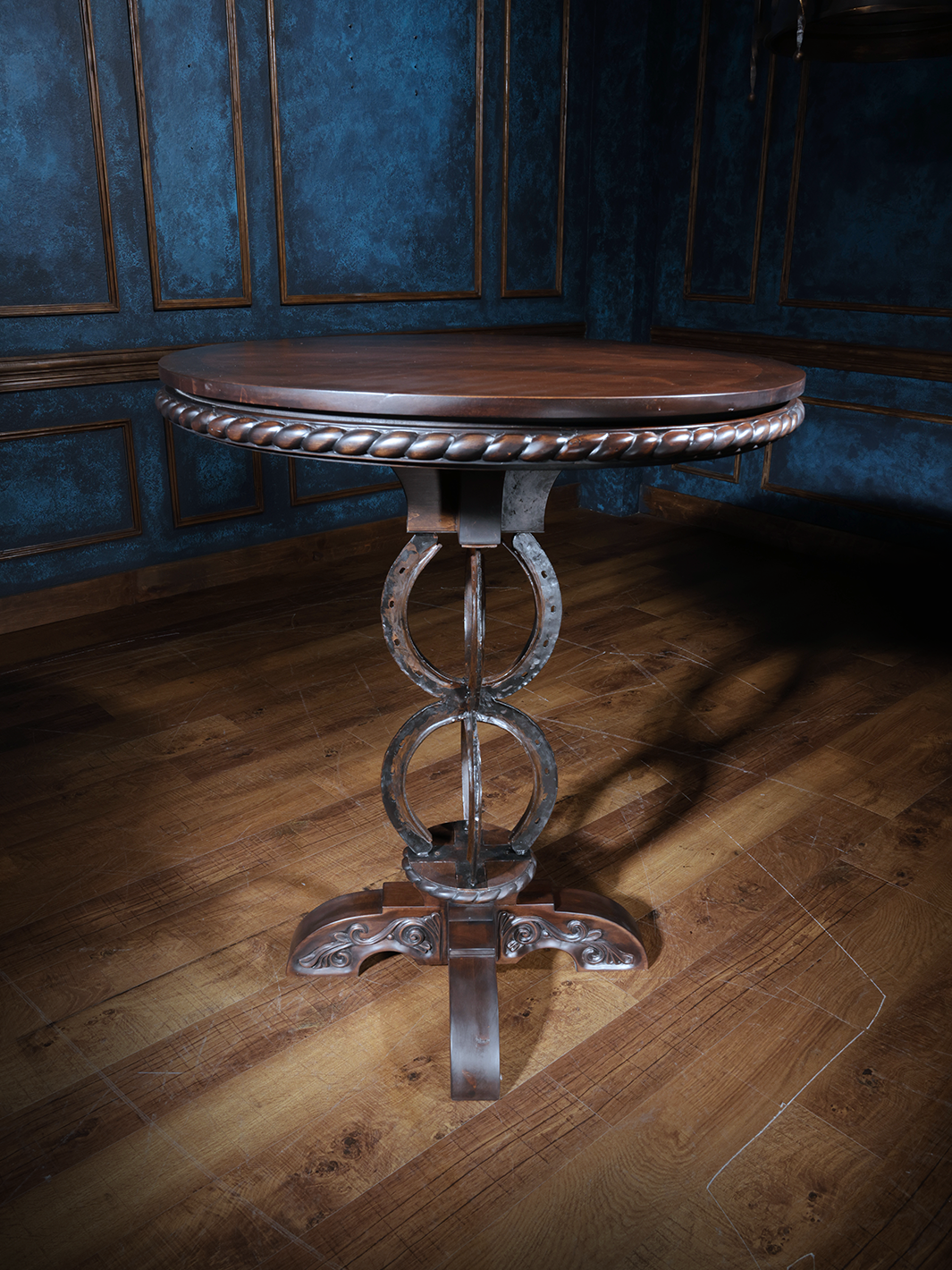 A rustic-style brown pub table with a horseshoe design on the base and carved detailing on the top, set against a dark blue background.