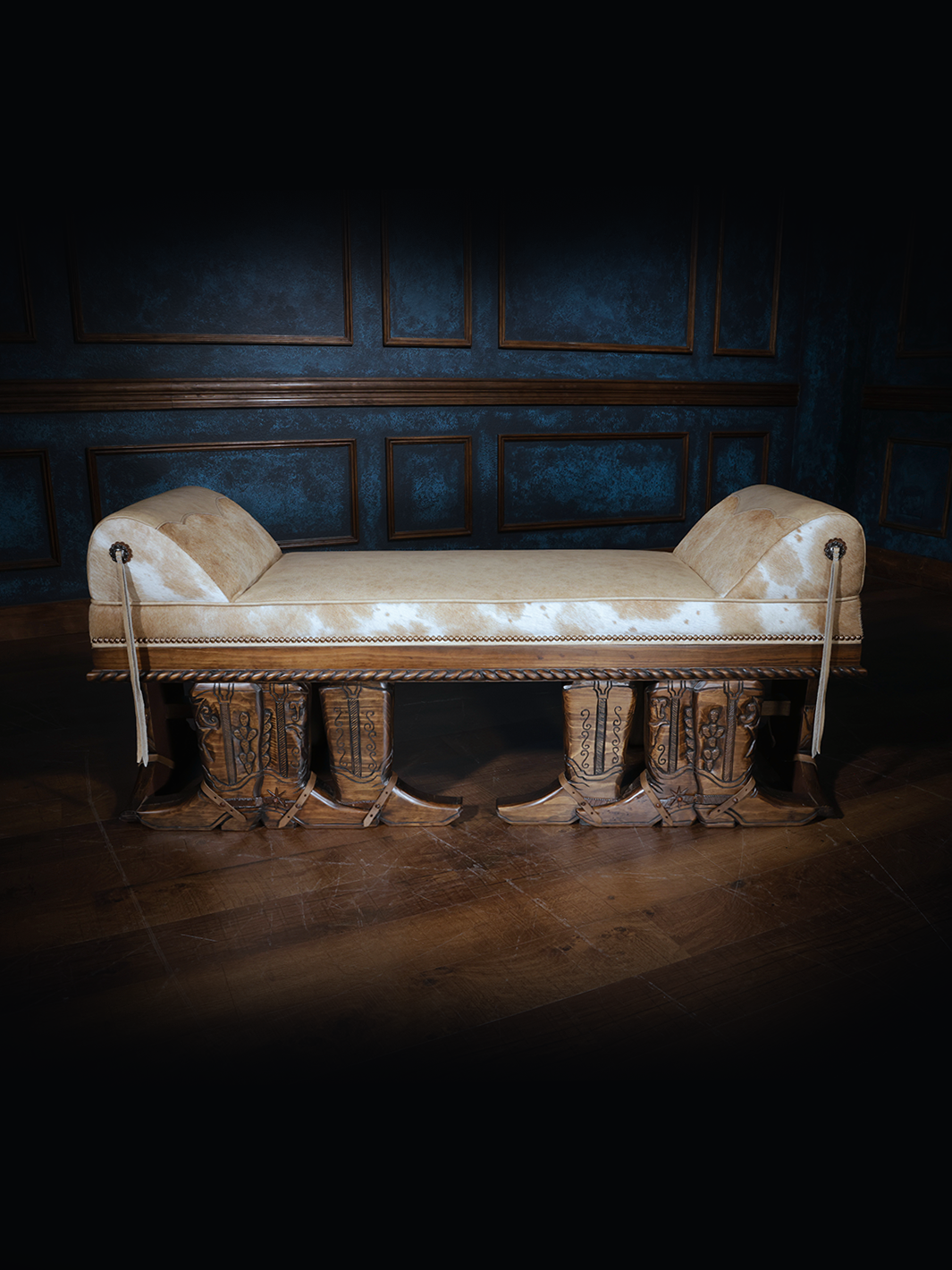 A bench with a blonde brindle cowhide seat and hand carved cowboy boot trim, set against a blue-painted wall with wooden flooring.