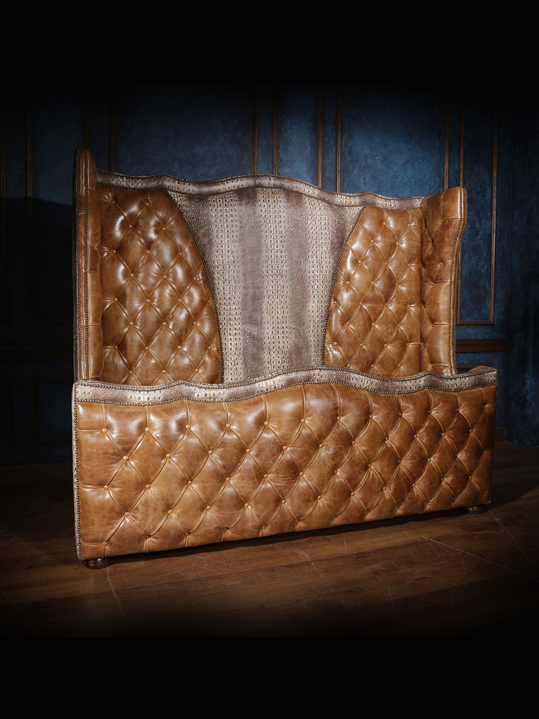 A brown tufted leather bed with crocodile patterned headboard and footboard, set against a blue textured background.