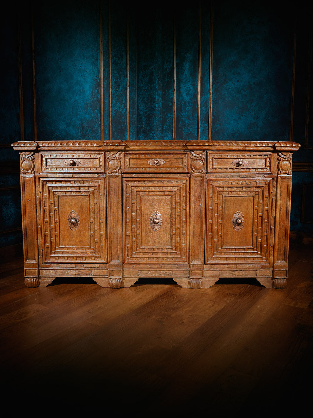 A wooden buffet sideboard with a rustic finish, featuring multiple drawers and cabinet doors, set against a blue backdrop.
