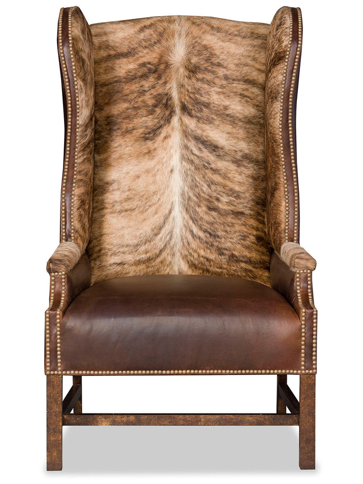 Front view of the Lexi Western Axis Accent Chair, featuring a high wingback design upholstered in genuine axis deer hide with a symmetrical spine pattern, paired with smooth brown leather on the seat and antique brass nailhead trim.