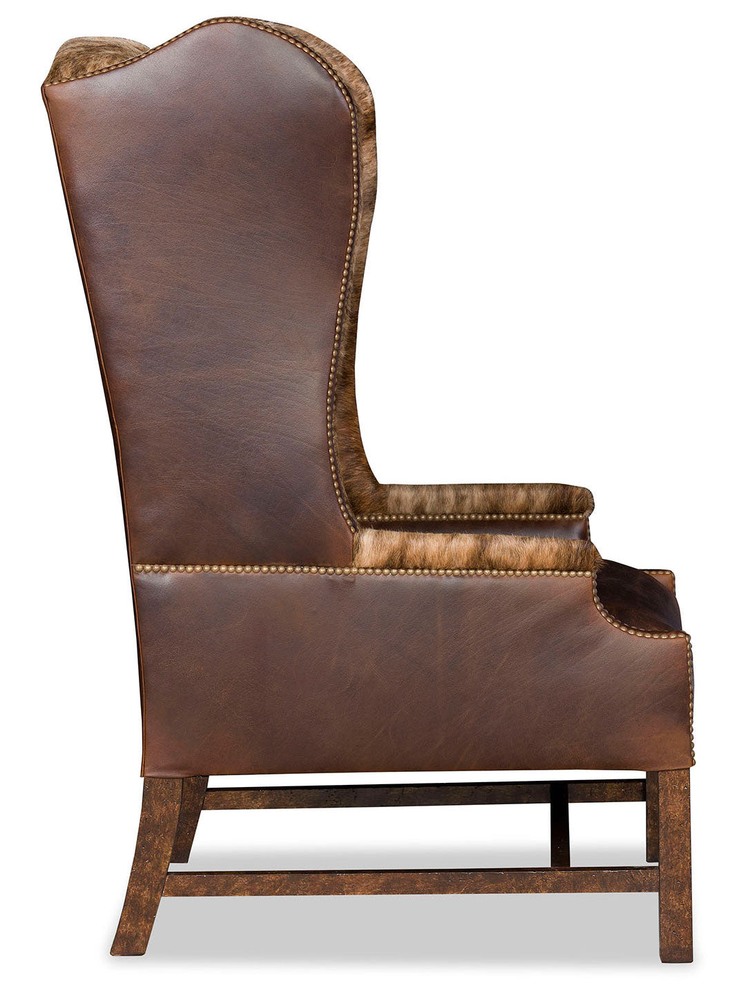Side profile of the accent chair showing the elegant curve of the wingback, leather upholstery, and nailhead accents along the edges, supported by a distressed wood frame.