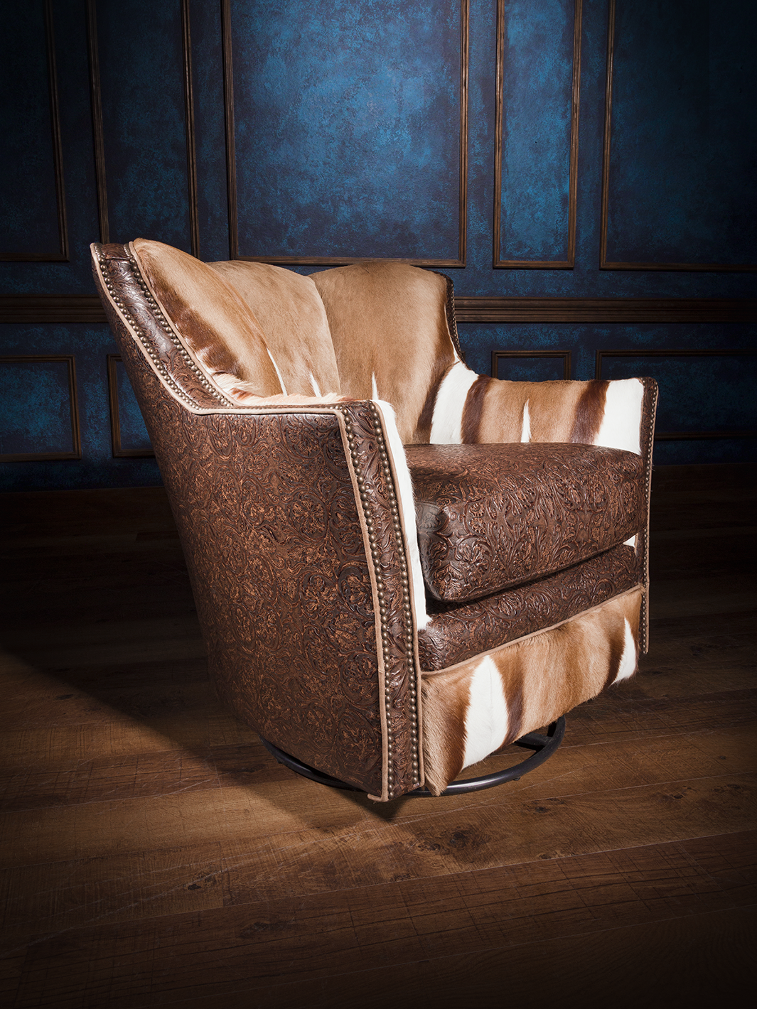 A brown and beige tooled leather swivel chair with a Springbok pattern, featuring nailhead trim, against a blue background.