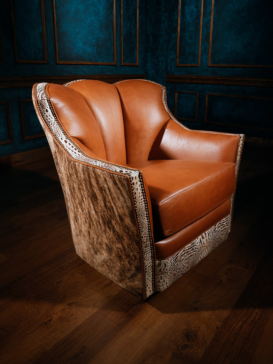 A brown swivel chair with a western caramel color leather cover, white croc-embossed trims, and grey brindle cowhide on the backrest, set against a blue panelled wall.