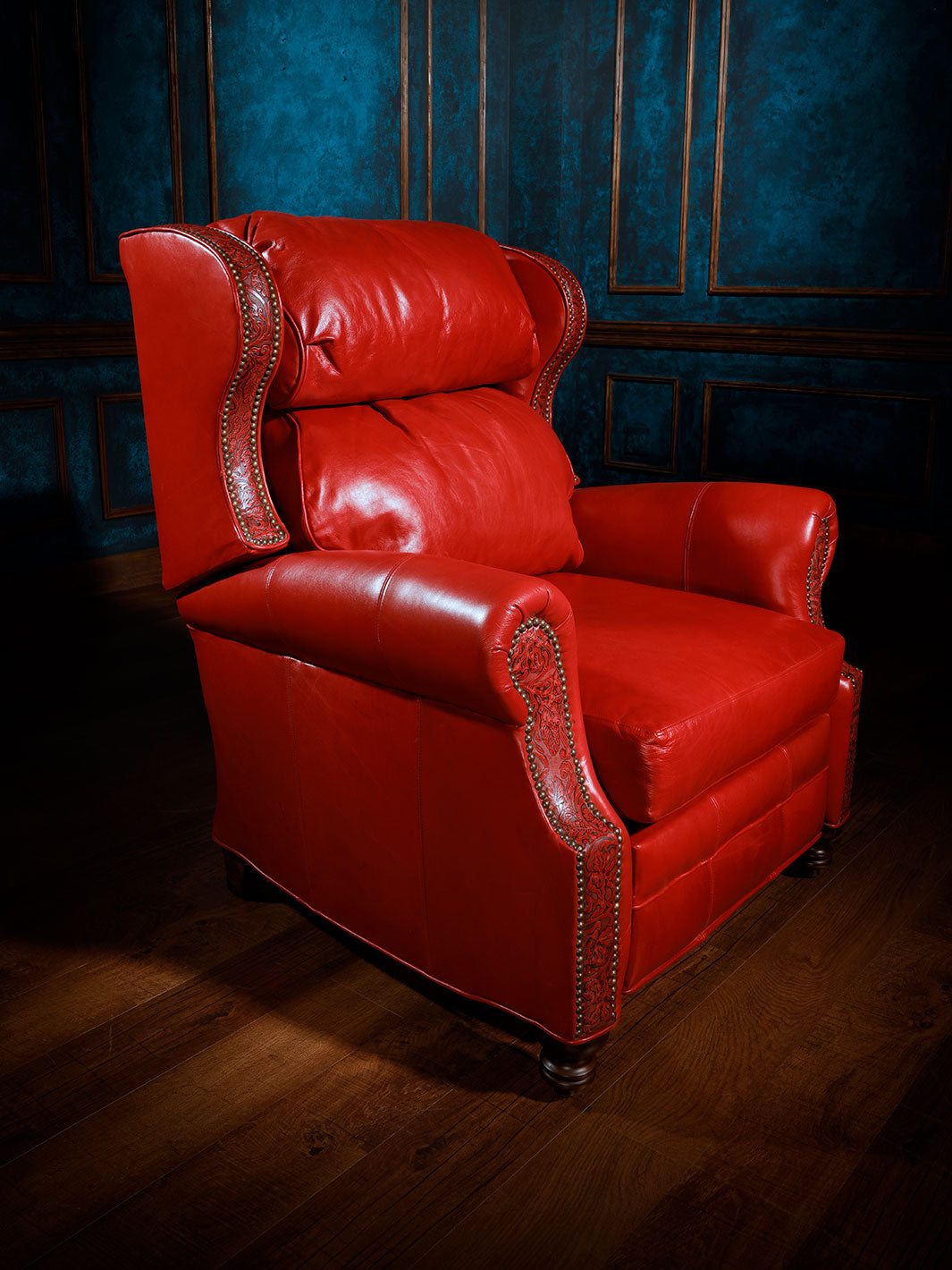 A luxurious red leather recliner chair with detailed trim and wooden legs, set against a blue upholstered wall.
