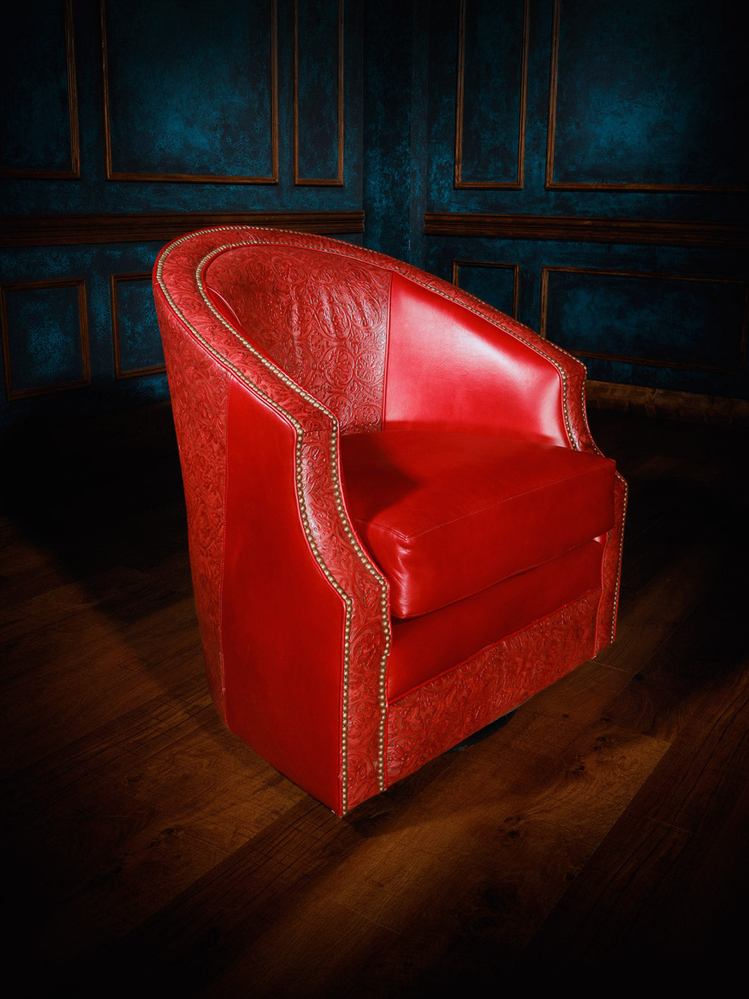 A red leather swivel chair with a cowboy tooled accent, displayed against a dark blue background with a wooden floor.