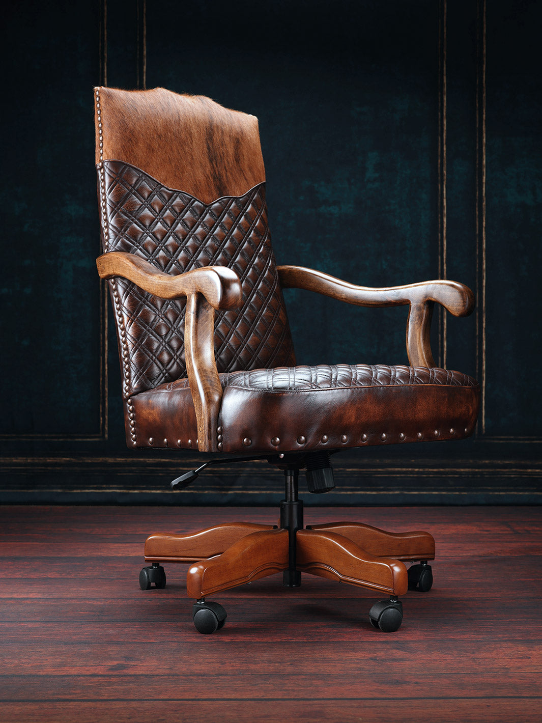 A brown quilted leather desk chair with a wooden frame and diamond pattern, situated on a dark floor against a dark background.