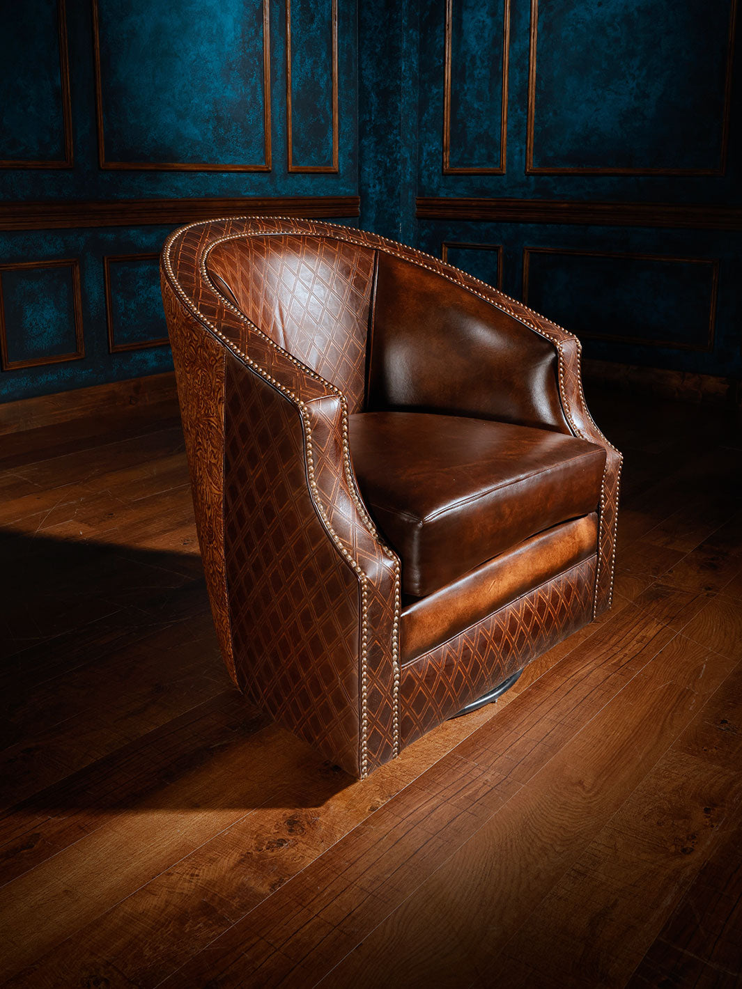 A brown leather swivel chair with a Cowboy Tooled accent, placed on a wooden floor with a blue paneled wall in the background.