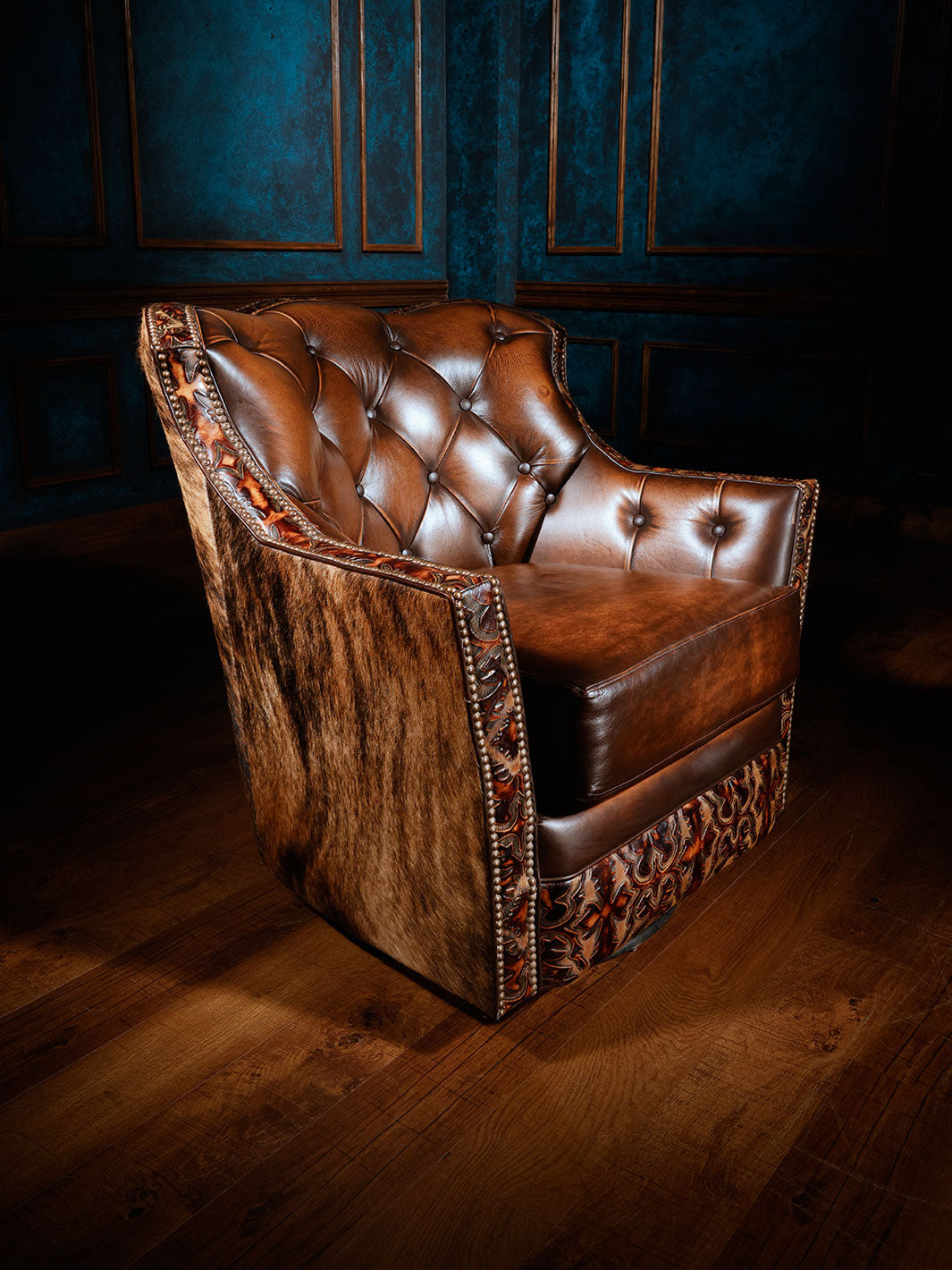 A brown leather swivel armchair with tufted backrest and a dark cowhide accent on the back and arm, set against a blue wall.