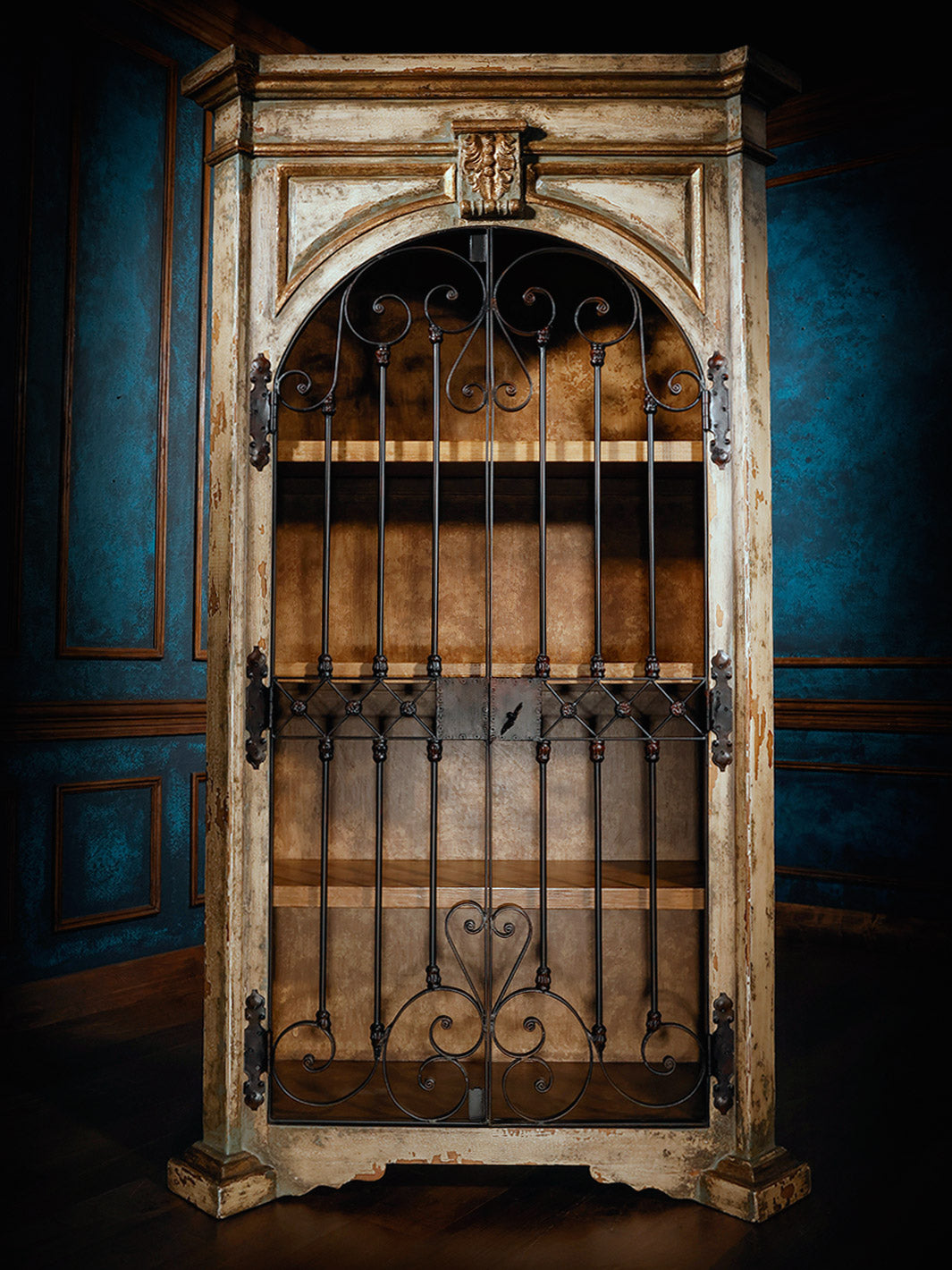 A wooden armoire with a painted finish and iron accents, featuring intricate carvings and a closed door.