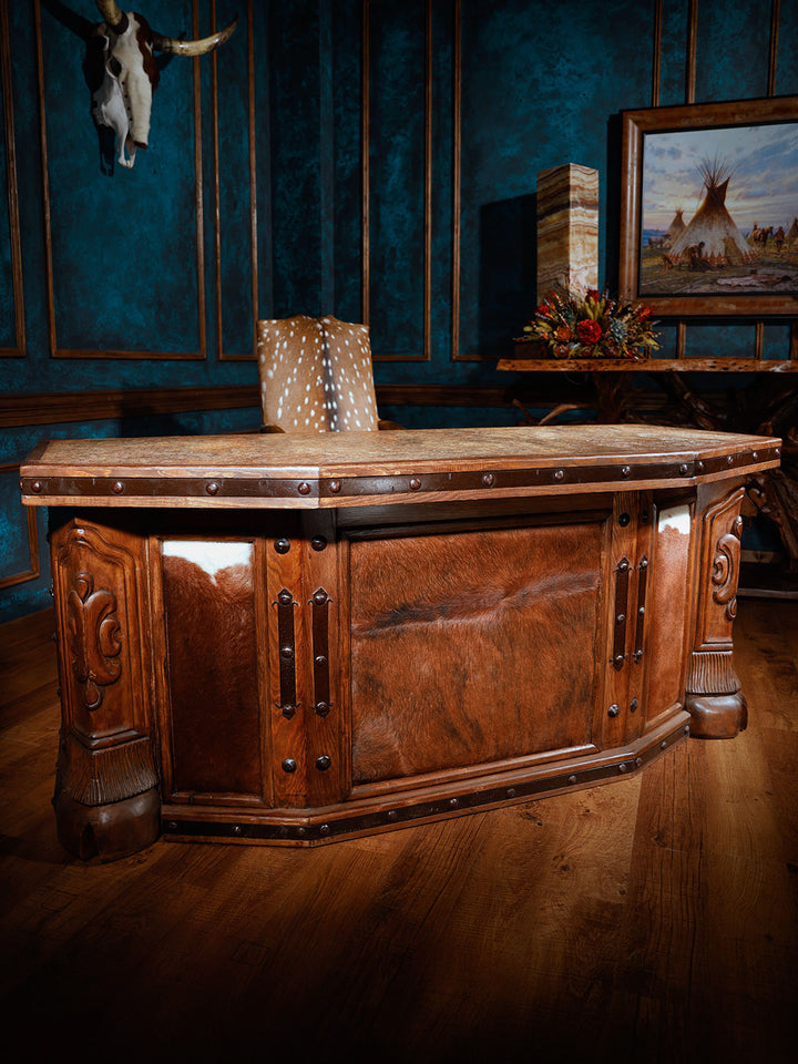 A hand-carved wooden desk with cowhide panels and a granite marble top, featuring five drawers, situated in an office setting.