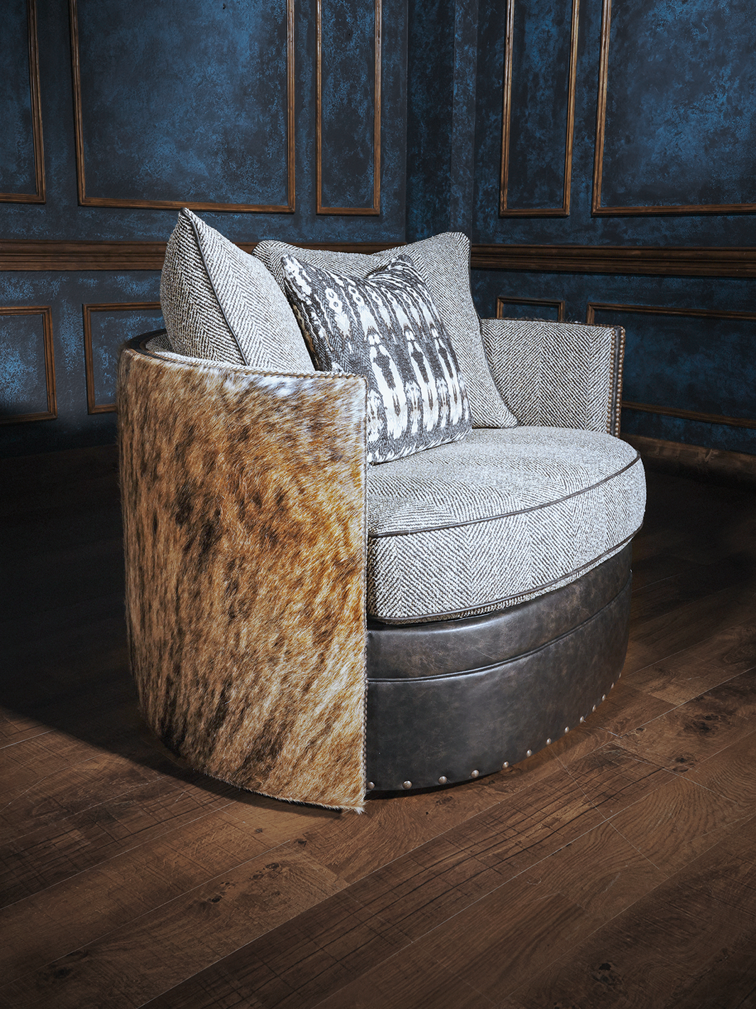 A swivel chair with a cowhide backrest and a cushioned seat and backrest, placed in a room with blue panelled walls.