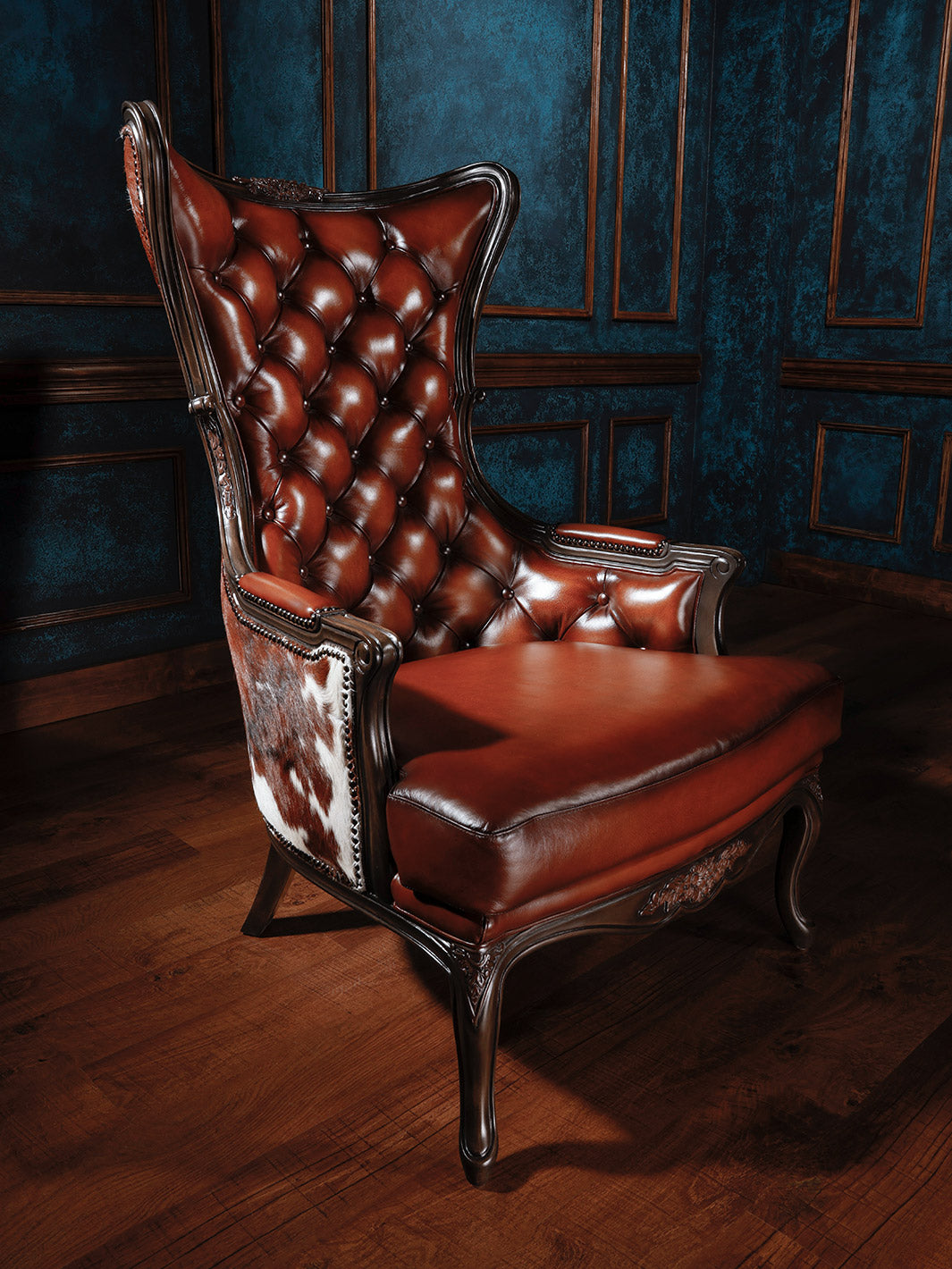 A brown leather accent chair with tufted buttons and cowhide accents, positioned in a room with blue paneling.