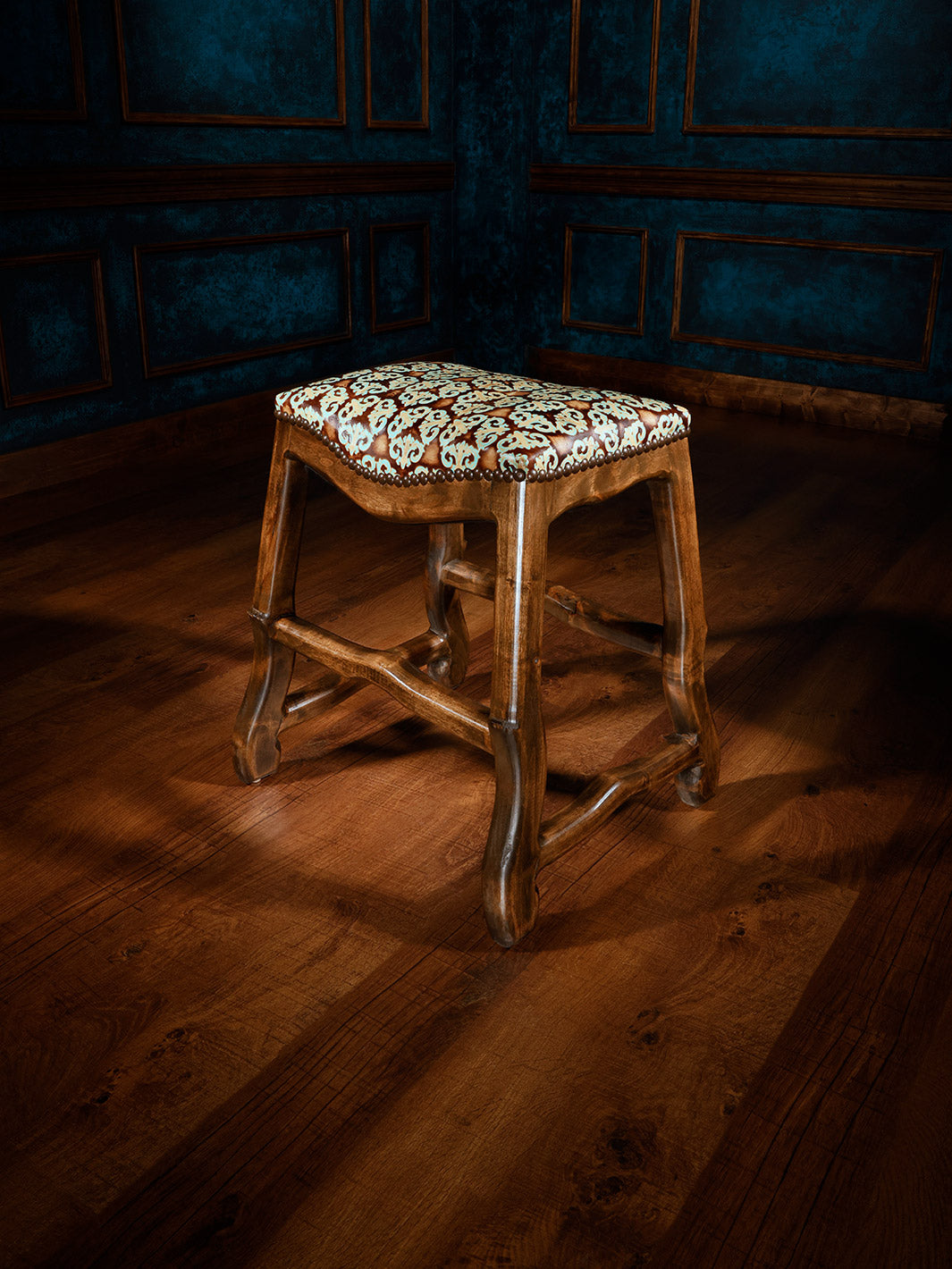 A tooled leather saddle stool with alderwood frame and polished chestnut finish, featuring brown distress marks and an embossed pattern on the seat.