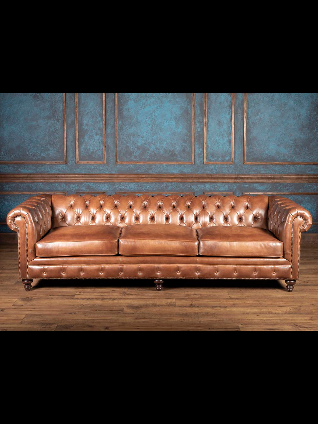 Almond burnished leather Chesterfield sofa with deep button tufting, rolled arms and nailhead trim in a blue paneled living room