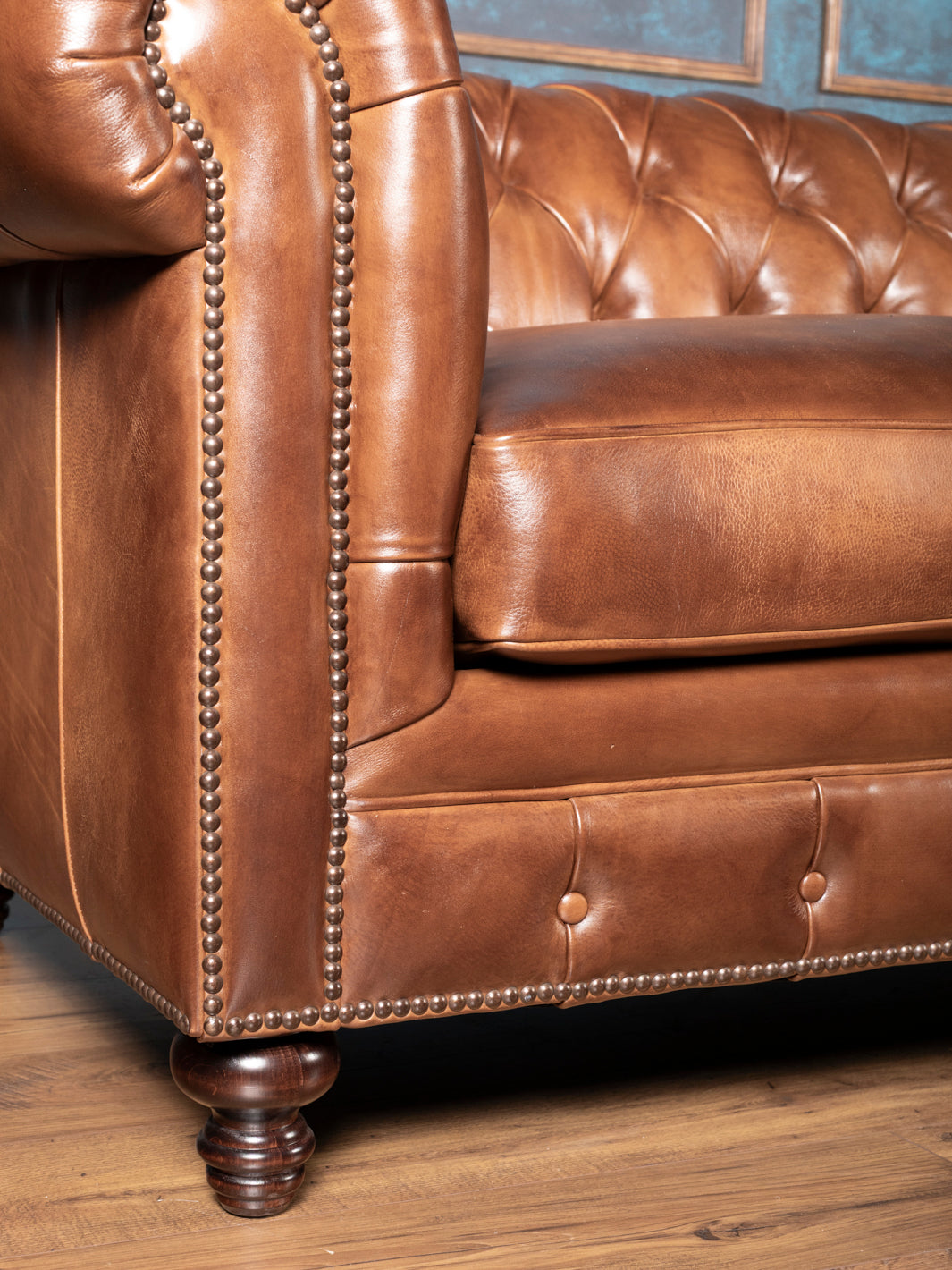 traditional leather Chesterfield sofa detail showing turned wood leg, plush seat cushion and studded nailhead front rail