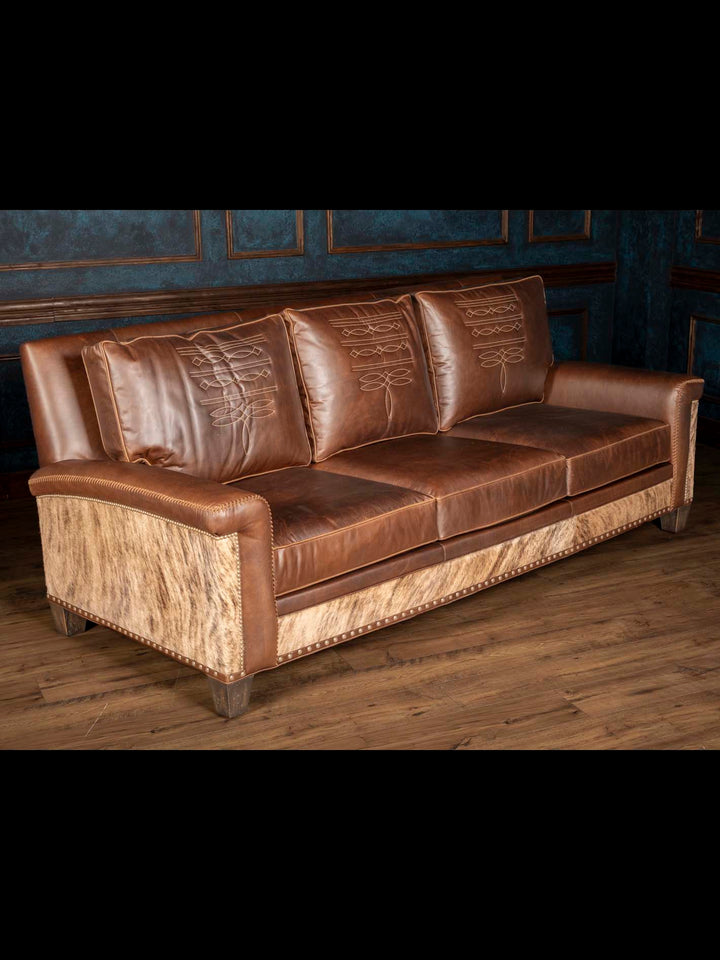 Angled view of authentic brown western leather sofa with cowhide accents and western detailing.