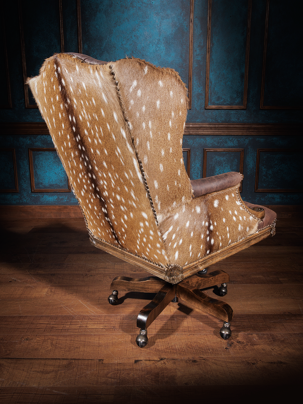 Back view of an office chair upholstered in axis hide with a wooden swivel base and casters, accented by nailhead trim and brown leather.