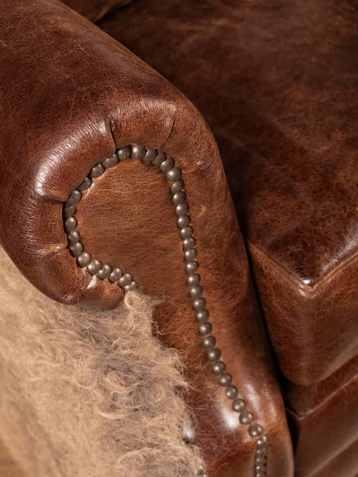 Close-up of a brown leather recliner rolled arm and antique nailhead accents