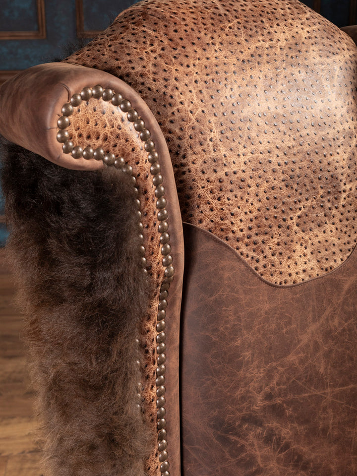 Close-up of a brown leather armchair with buffalo and studded details.