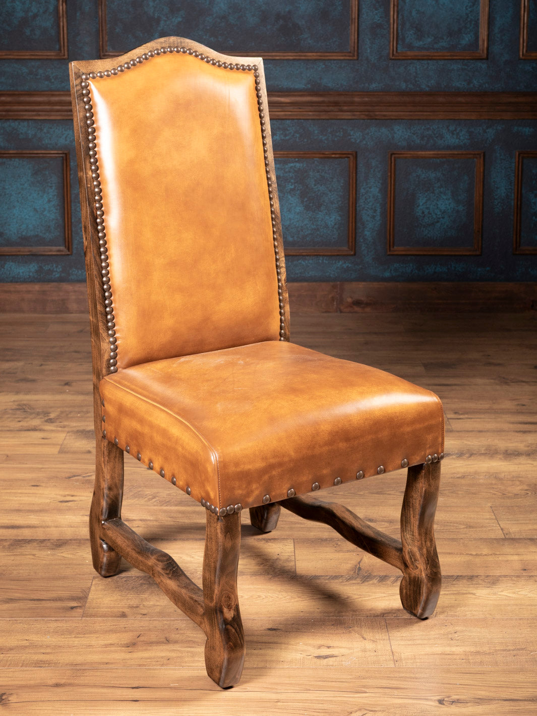 Brown leather chair with wooden legs against a blue wall.