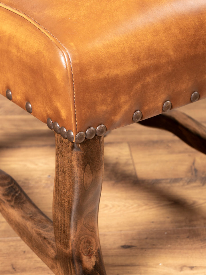 Close-up of a brown leather chair with metal studs on a wooden floor.