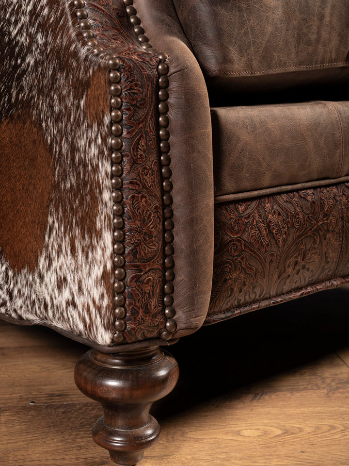 Brown leather sofa with cowhide pattern and wooden legs on a wooden floor.