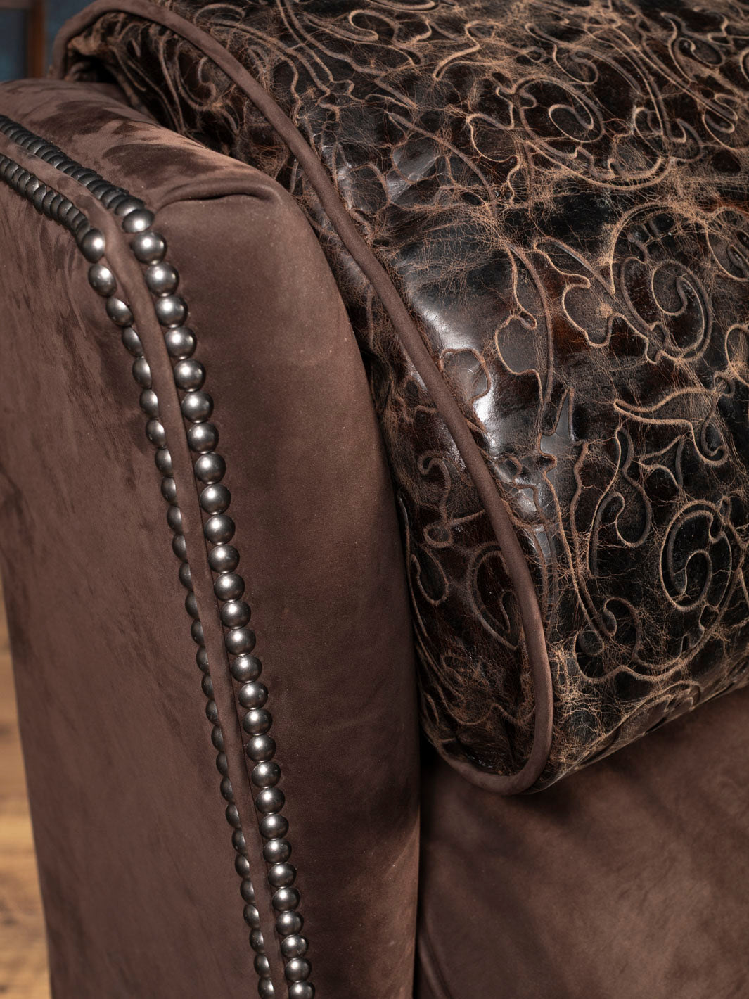 Close-up of a brown leather recliner with tooled leather and nailhead accents