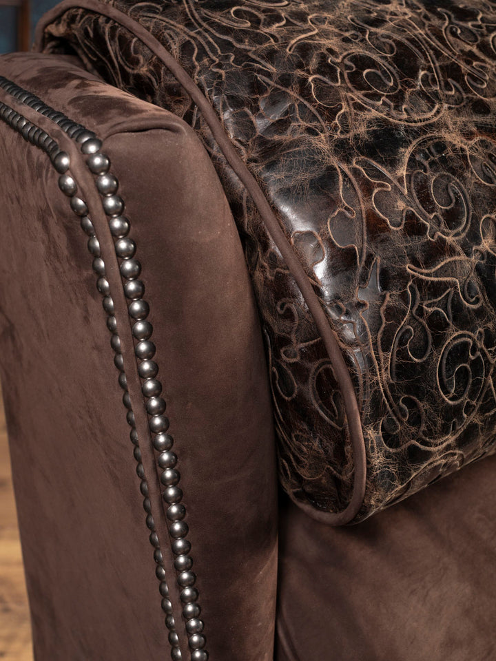 Close-up of a brown leather recliner with tooled leather and nailhead accents