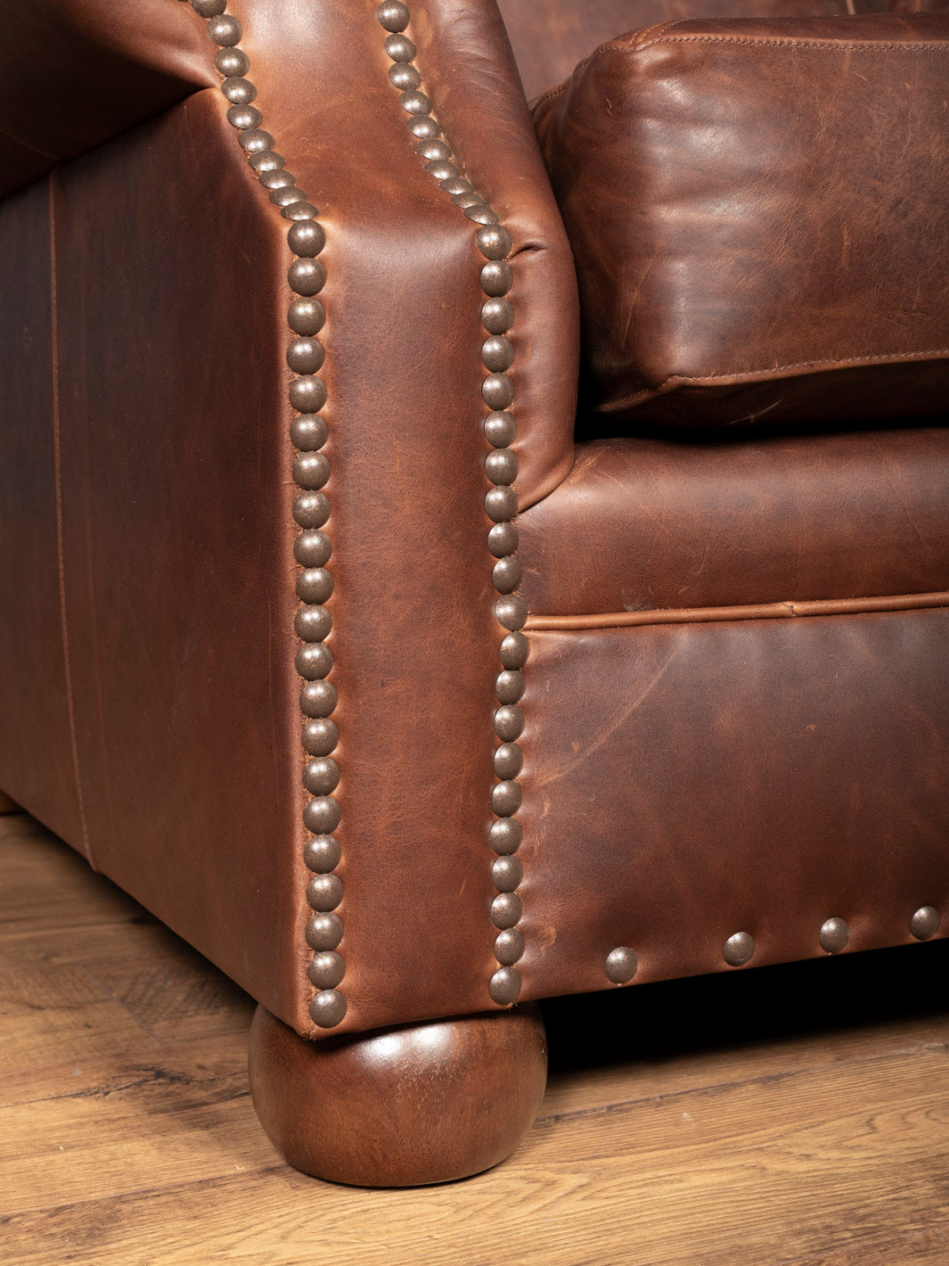Brown leather sofa with nailhead trim on a wooden floor