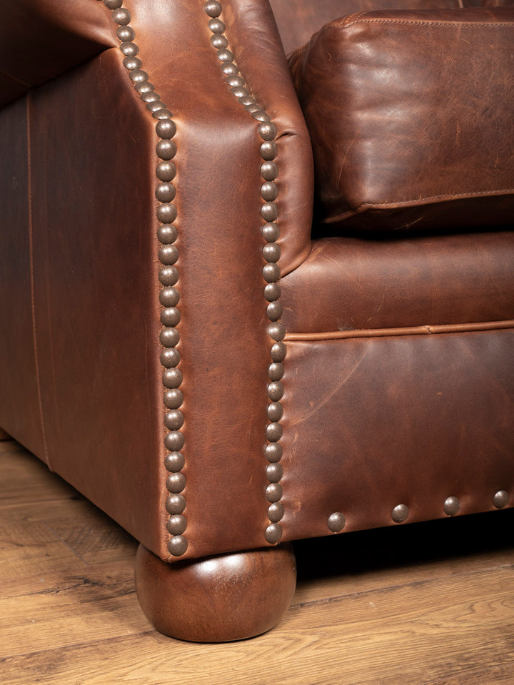 Brown leather sofa with nailhead trim on a wooden floor