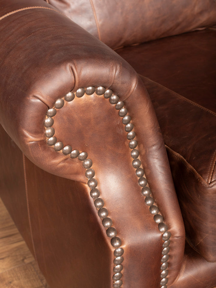 Close-up of brown leather rolled arm of sofa with decorative nailhead trim.