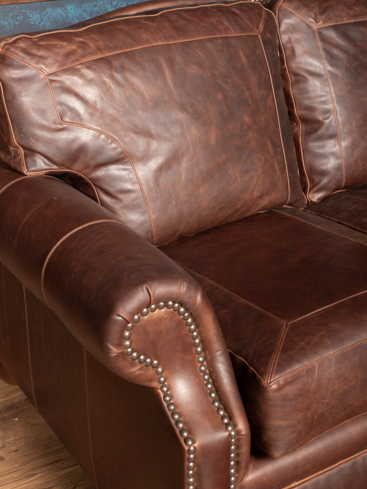 Brown leather sofa with nailhead trim on a wooden floor.