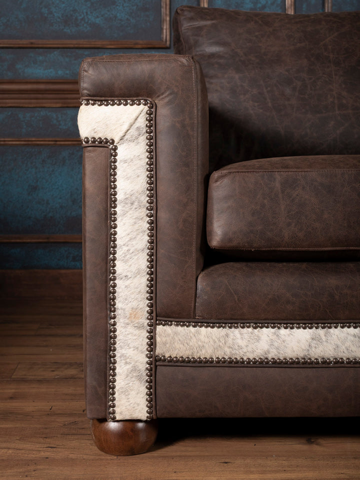 Close-up of arm detail showing embossed leather trim, gray cowhide, and nailhead accents