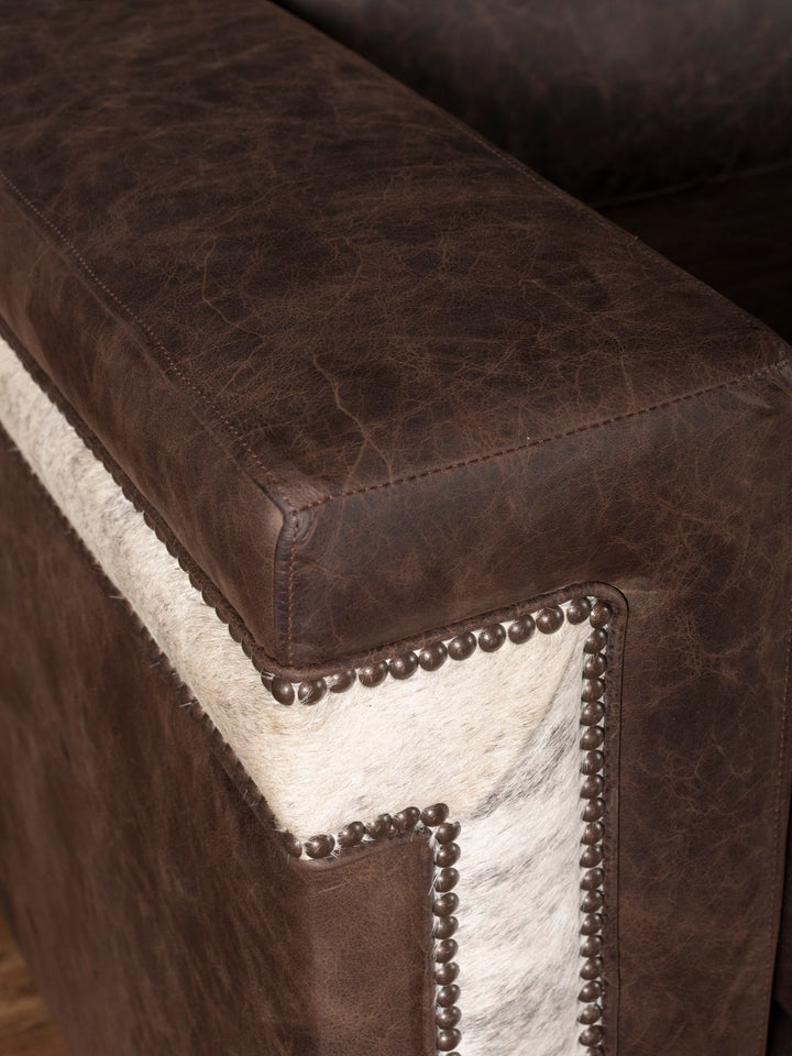 Close-up of a brown leather sofa with cowhide accents and nailhead trim