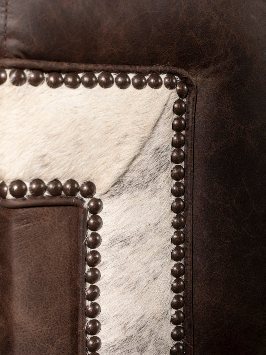 Close-up of a leather sofa with nailhead trim and cowhide pattern.