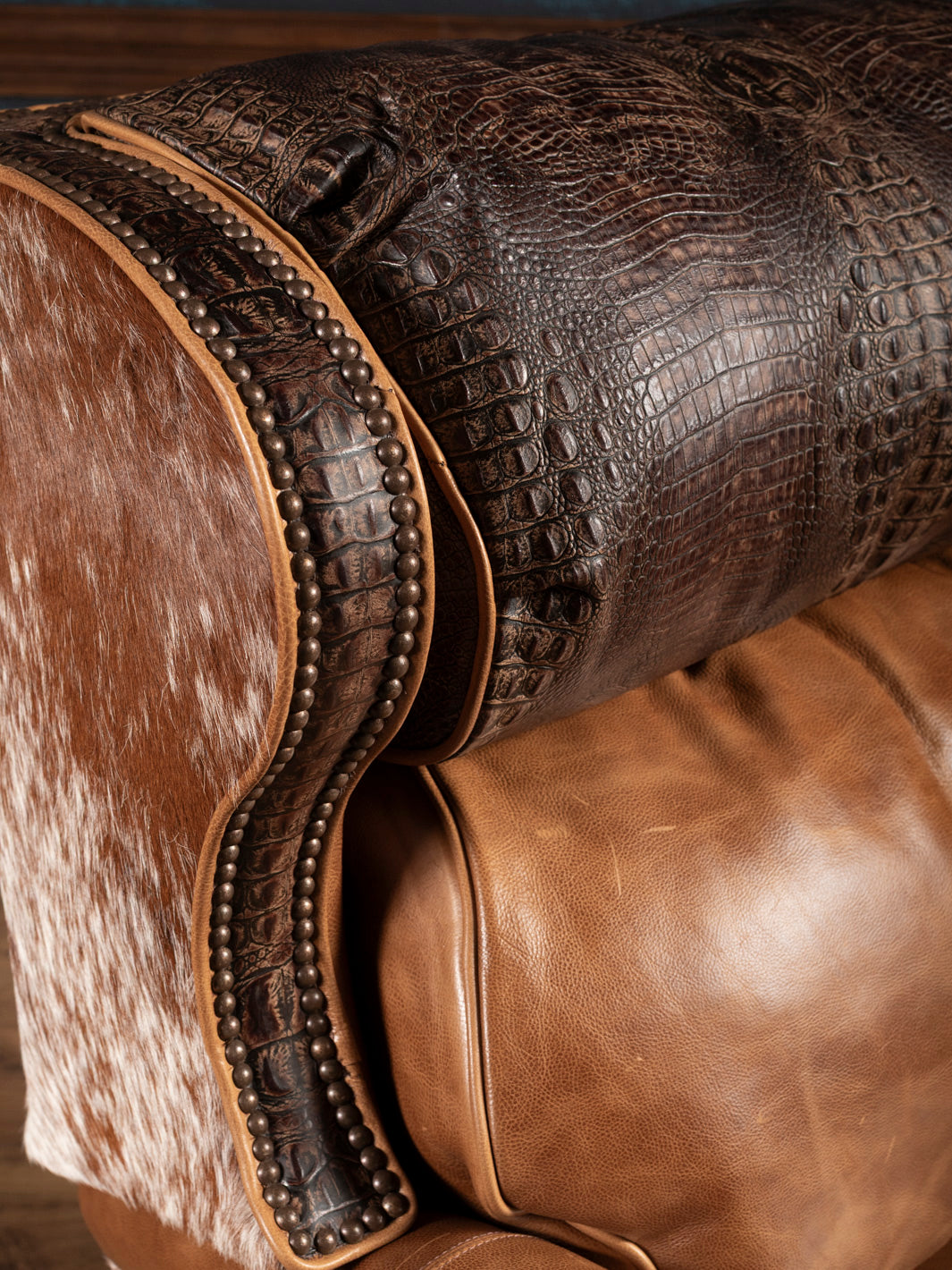 Close-up of headrest and wingback detail featuring crocodile-embossed leather, smooth saddle leather, nailhead trim, and brindle cowhide.