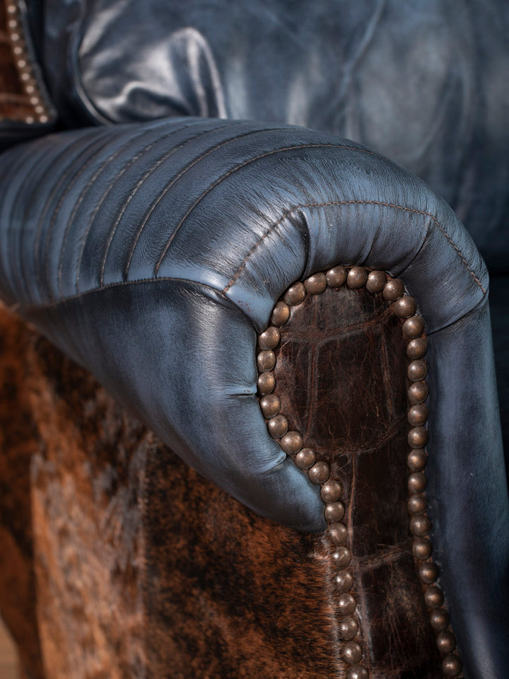 Detailed shot of Western recliner with curved rolled arm, blue leather quilting, nailheads, and brindle cowhide upholstery