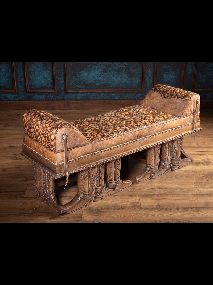Western-style bench with leather and patterned fabric, supported by cowboy boot-shaped carved wooden legs.