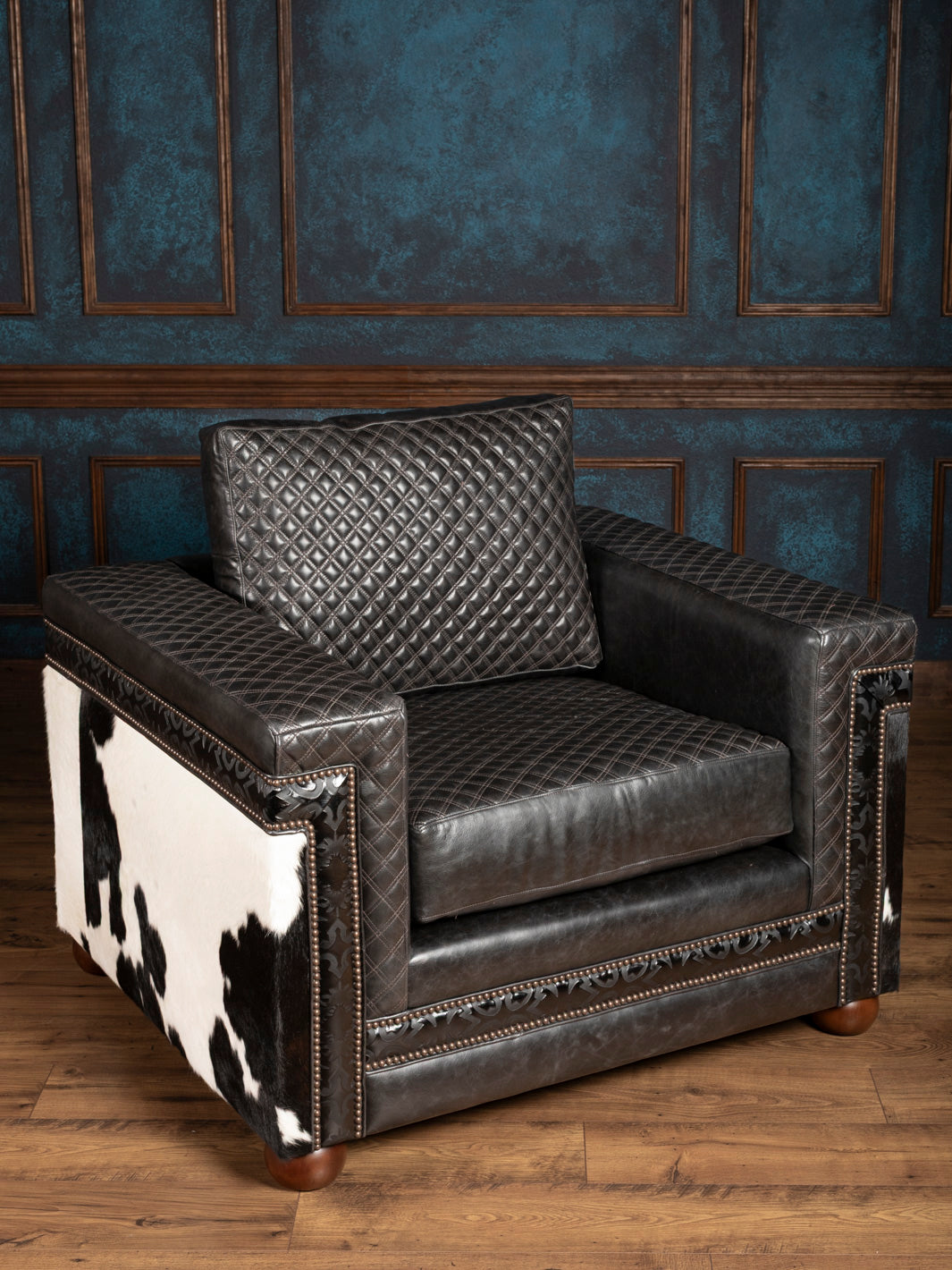 Black leather armchair with cowhide pattern on a wooden floor against a blue paneled wall.