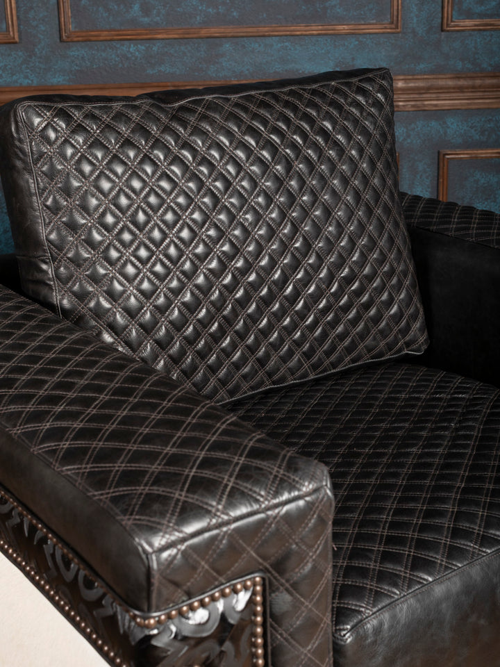 Black quilted leather sofa with decorative pillows against a blue wall.