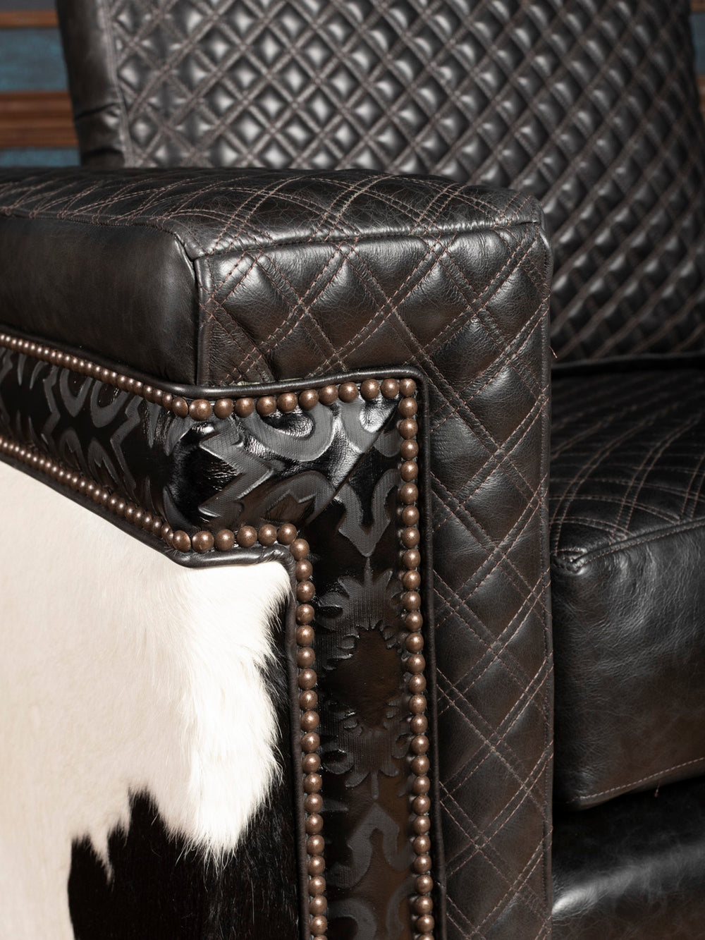 Close-up of a black leather armchair with decorative stitching and nailhead trim.