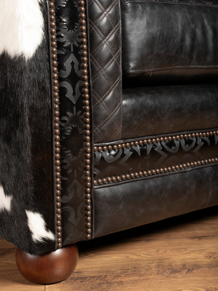 Close-up of a black and white cowhide armchair with decorative nailhead trim on a wooden floor.