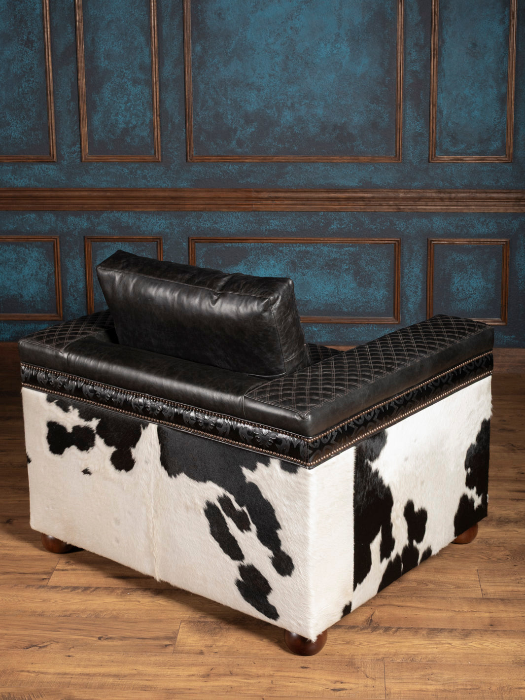 Black and white cowhide chair with leather top against a blue paneled wall.